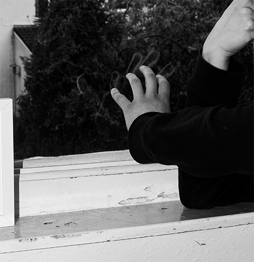 Black and white DSLR image of a hand touching a window with a smudge mark of condensation marking where the hand has fallen. through the window is a blurred vision of tress.